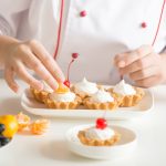 Professional female confectioner decorating mini fruit tarts
